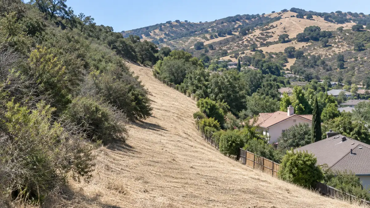 Cleared fire break cut through dry brush along the open hillside boundary above a Chino Hills neighborhood