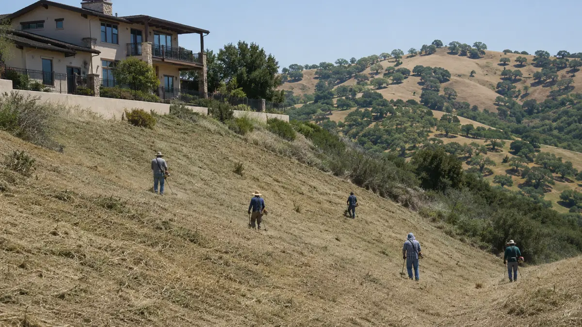 Land clearing crew working a long back slope below a large hillside home in Diamond Bar, California, with the open Tonner Canyon hills beyond